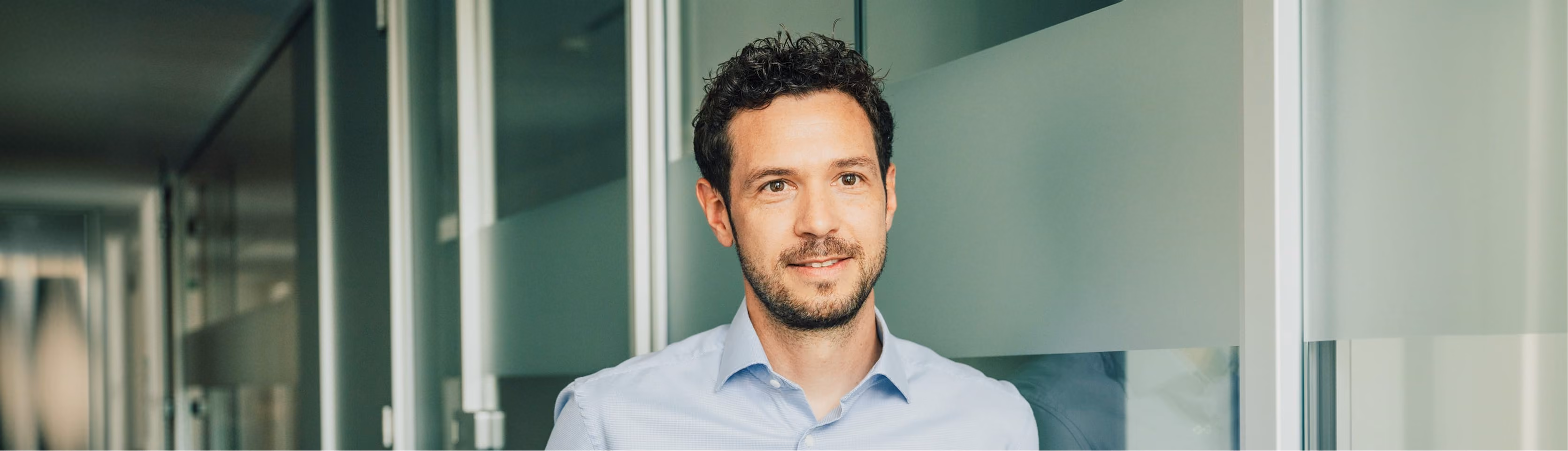Zwei Männer betrachten gemeinsam etwas außerhalb des Bildes in einem modernen Büro mit Glaswänden.