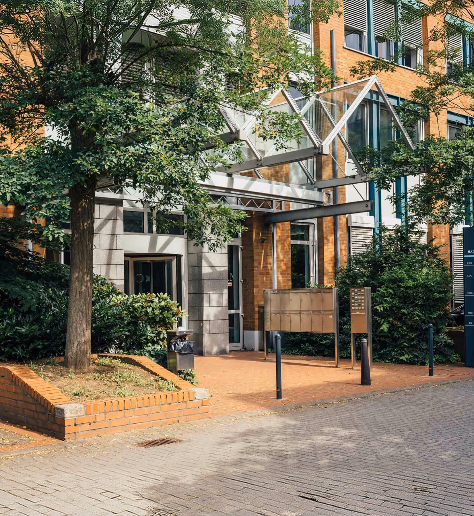 Eingang eines Bürogebäudes mit Glaspavillon, Briefkästen und Bäumen in Düsseldorf.