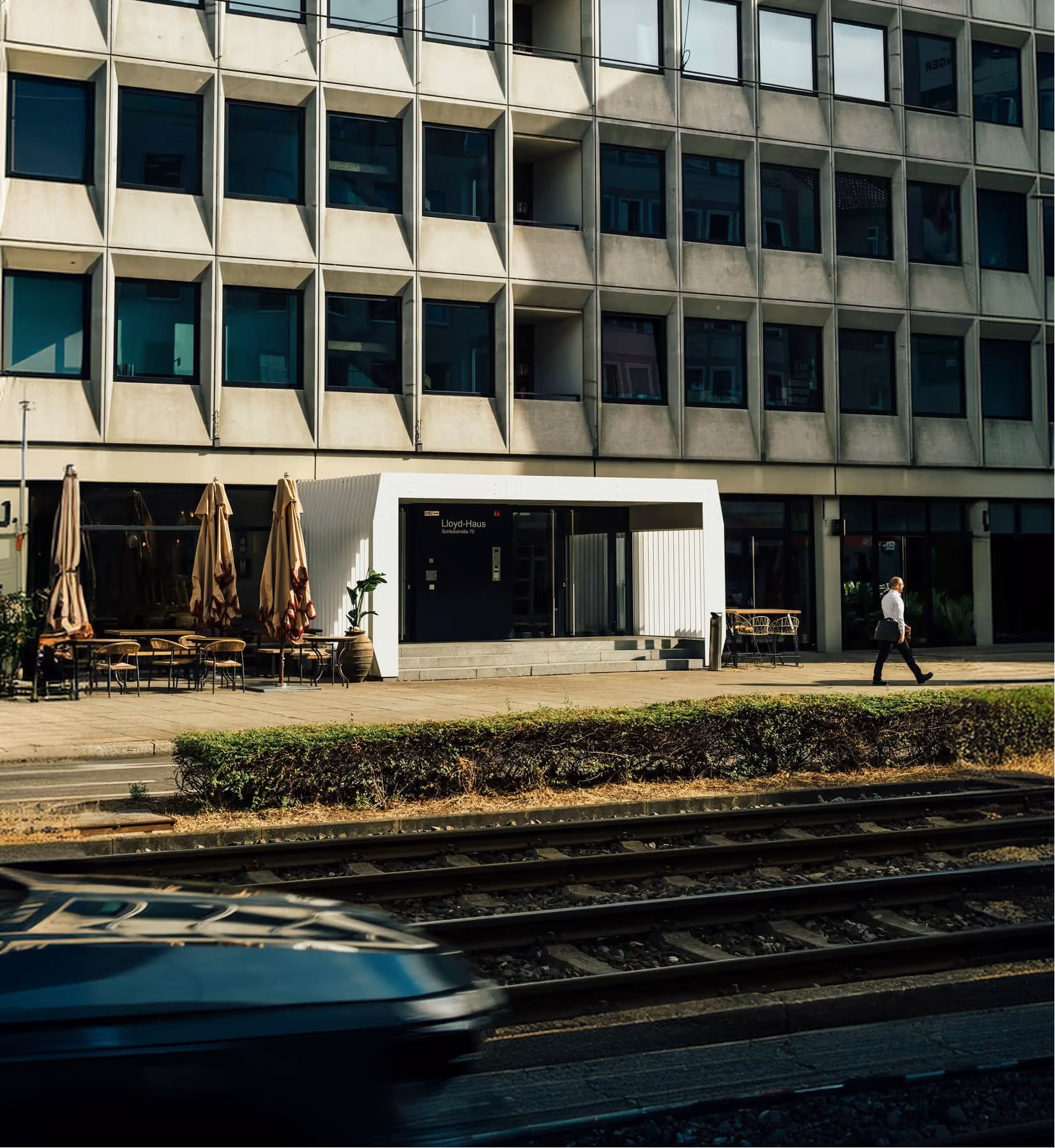 Ein Mann mit Aktentasche geht vor dem Lloyd-Haus mit Tischen und geschlossenen Sonnenschirmen in Stuttgart.