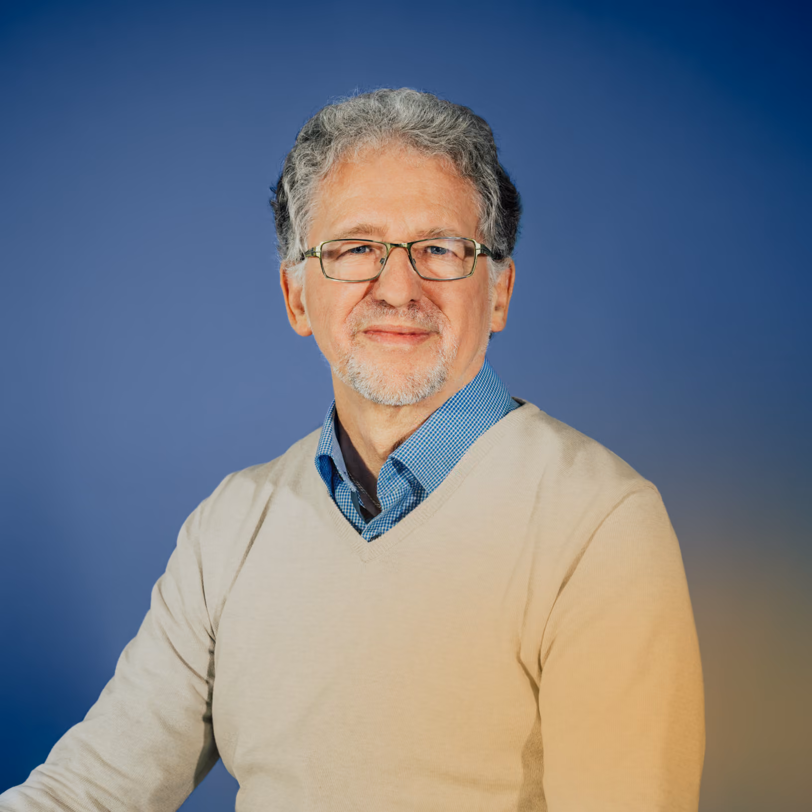 Älterer Mann mit grauem Haar, Brille und hellem Pullover vor blauem Hintergrund.